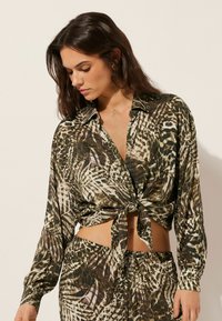 Blusa de manga corta con nudo que presenta un estampado animal multicolor en verdes, marrones y blancos. Material ligero y sedoso con cuello.