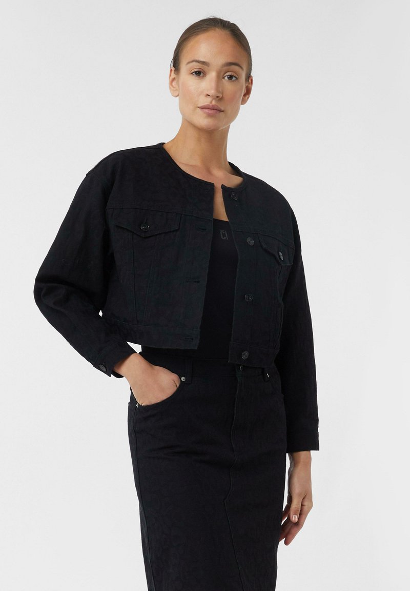 Black denim jacket with a cropped design, featuring a round neckline, button closure, and two chest pockets. Subtle textured leopard pattern.