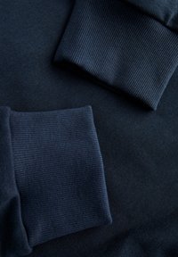 Sudadera de un oscuro color navy con puños acanalados y una textura del cuerpo suave. La tela es suave y se estira ligeramente para mayor comodidad.