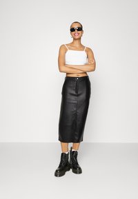 Mustleather midi-seelik peene disainiga, nööpide sulgemisega, kombineeritud valge lühikese ülemisega ja mustade paeltega saapatega. Aksessuaaride hulka kuuluvad prillid.