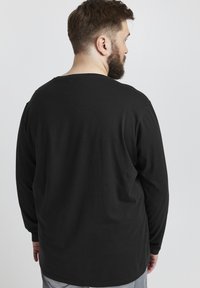 Long-sleeve black t-shirt made of cotton with a round neckline. Features a relaxed fit and smooth texture. Clean, simple design.
