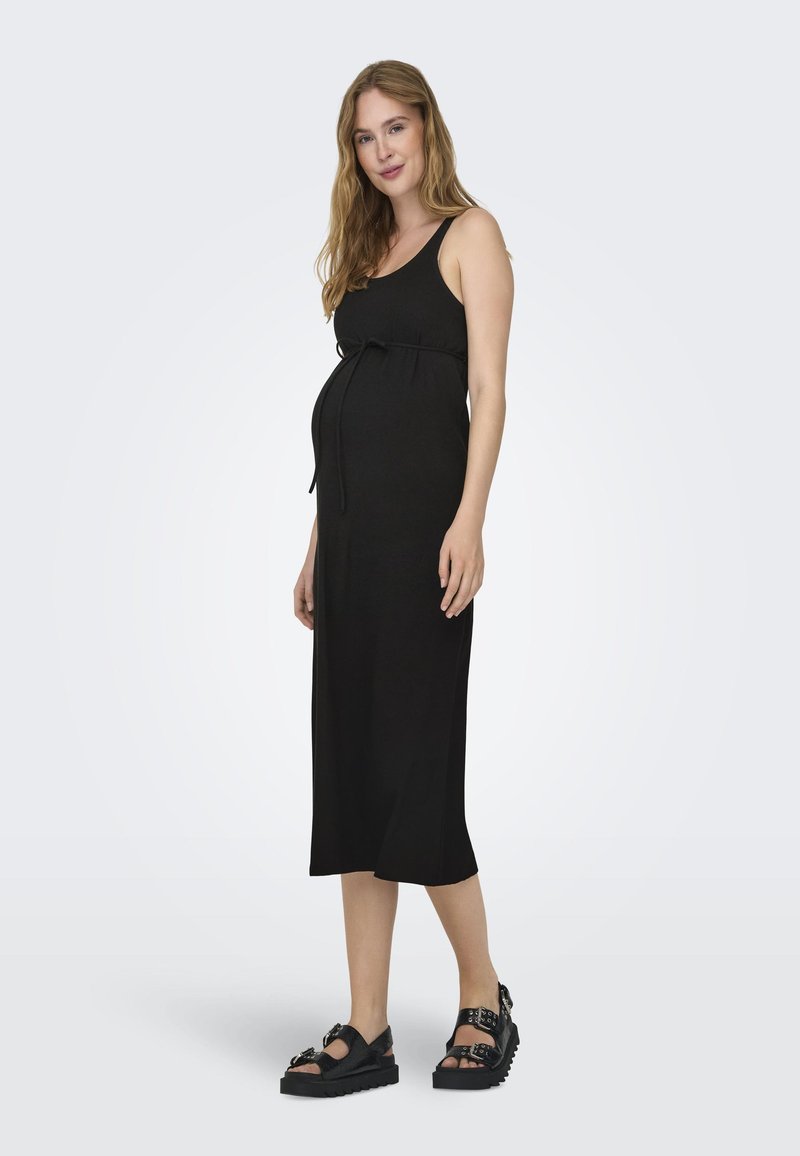 Robe de maternité noire avec un corsage ajusté, une ceinture à la taille réglable et une jupe mi-longue et fluide. Associée à des sandales noires épaisses.