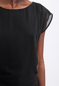 Blouse noire en tissu lisse, avec un col rond et des manches courtes en dentelle. Présente une coupe décontractée et un design minimaliste.