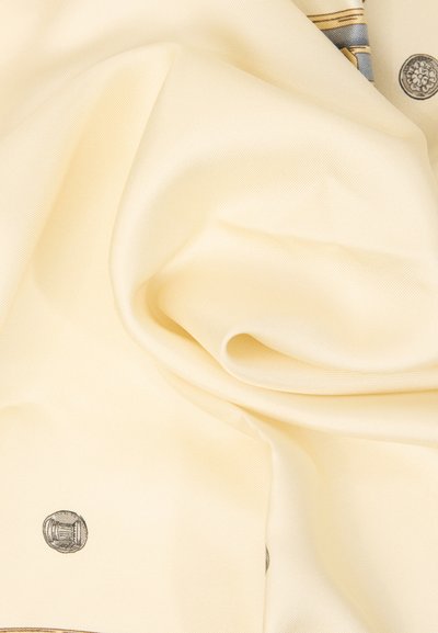 Υφασμα σε κρεμ απόχρωση με λεπτές πτυχές, διακοσμημένο με μικρά κυκλικά σχέδια και μια ελαφριά ένδειξη ριγέ και λουλουδένιων μοτίβων κοντά στην πάνω άκρη.