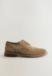 Beige mokassinsi suédë kengät, joissa on siipikuvio, brogue-reikätyöt ja litteat kumipohjat. Varustettu kuudella silmäreijällä ja kontrastivärisellä ompelella.