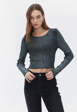 Crop top z długimi rękawami, o prążkowanej fakturze i wielokolorowym połysku. Połączony z czarnymi jeansami z wysokim stanem, z zapięciem na guzik.