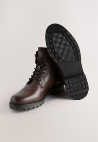 Braune Leder-Schnürstiefel mit rundem Zehenbereich, kontrastierender, strukturierter Sohle und gepolstertem Knöchelbereich. Mit Ösen und Logodetail.