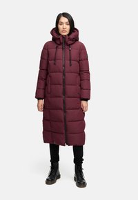 Cappotto puffer lungo bordeaux con cappuccio, design a righe orizzontali, due tasche laterali e zip frontale, abbinato a pantaloni neri e stivali.