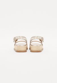 Espadrille-lignende sandaler med en beige tekstiloverdel, justerbar ankelrem og flettet jute platåsål. Glatte, strukturerte detaljer.