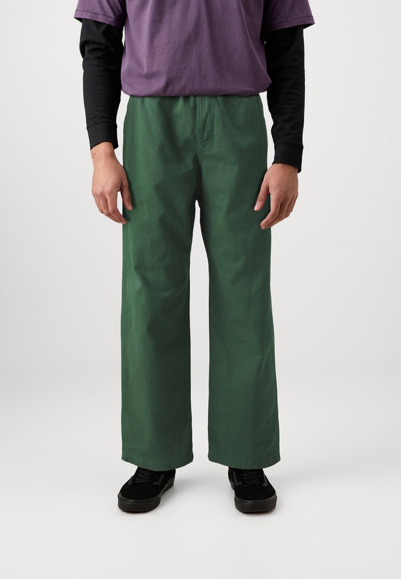 Groene wijde broek van een katoenmix, met een soepele textuur en een losse pasvorm. Gecombineerd met een paars en zwarte gelaagde top.