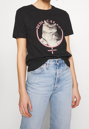 Osoba nosząca czarny T-shirt z szarym kotem wewnątrz różowego symbolu kobiety oraz napisem "DEDICATED PUSSIES UNITE", w połączeniu z jasnoniebieskimi dżinsami.