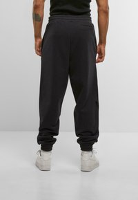 Mørkegrå sweatpants lavet af blødt stof, med elastisk talje, tapered manchetter og en baglomme. Parret med hvide sneakers.