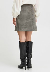 Aukštai užsegama sijonas su check tipo raštu, sukurtas pastelinių atspalvių, derinamas su juodais odiniais batais iki kelių, turinčiais siaurus kulnus.