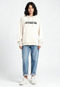 Felpa con cappuccio color crema con testo nero, tasca a marsupio e coulisse. Abbinata a jeans azzurri con risvolti e sneakers bianche.