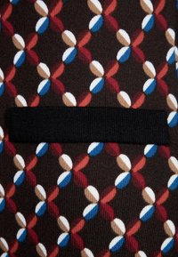 Tissu à motif présentant un design géométrique en rouge, bleu, blanc et marron sur un fond marron foncé ; comprend une bande d'accent noire.