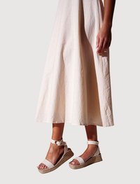 Kilesandaler med en sål af flettet jute, hvide stofstropper og en rund metalspænde. Designet med åben tå og ankelstøtte.