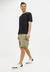 Sort bomulds T-shirt, kortærmet, parret med olivengrønne cargo shorts med klaplommer. Hvide sneakers med sorte detaljer.