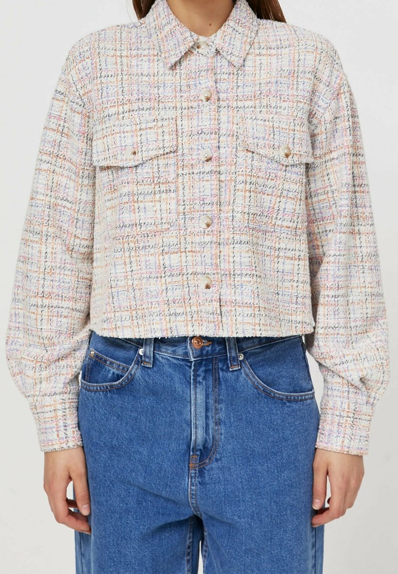 Veste courte boutonnée avec motif écossais multicolore pastel et poches poitrine à rabat, portée avec un jean bleu taille haute.