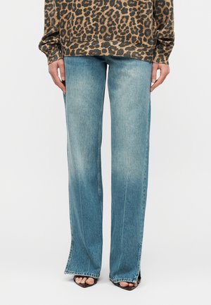 Άτομο που φορά φθαρμένα μπλε τζιν παντελόνια με φαρδιά μπατζάκια και σκισίματα μπροστά στο τελείωμα, σε συνδυασμό με μακρυμάνικο τοπ με μοτίβο λεοπάρ και μαύρες ανοιχτές γόβες.