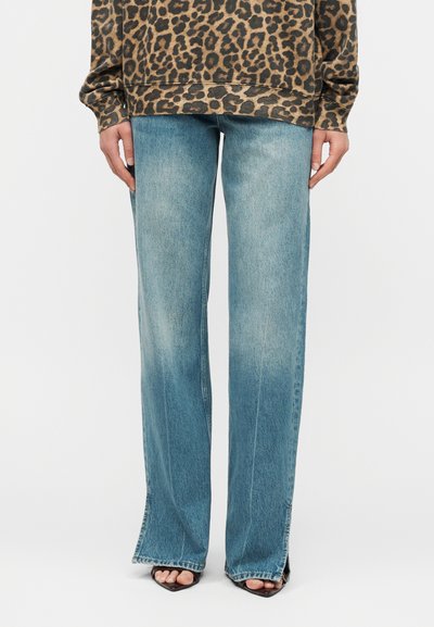 Personne portant un jean large bleu délavé avec des fentes à l'avant de l'ourlet, associé à un haut à manches longues à imprimé léopard et des talons ouverts noirs.