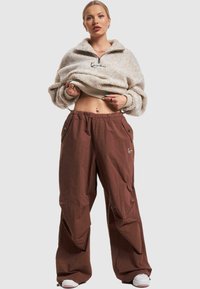 Fuzzy light beige zip-up fleece pullover, paired with loose-fitting brown cargo pants featuring side pockets and a drawstring hem.