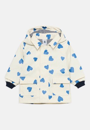 Pelerină de ploaie pentru copii, crem, cu modele albastre de inimă, glugă căptușită cu dungi, buzunare frontale și manșete bleumarin cu dungi.