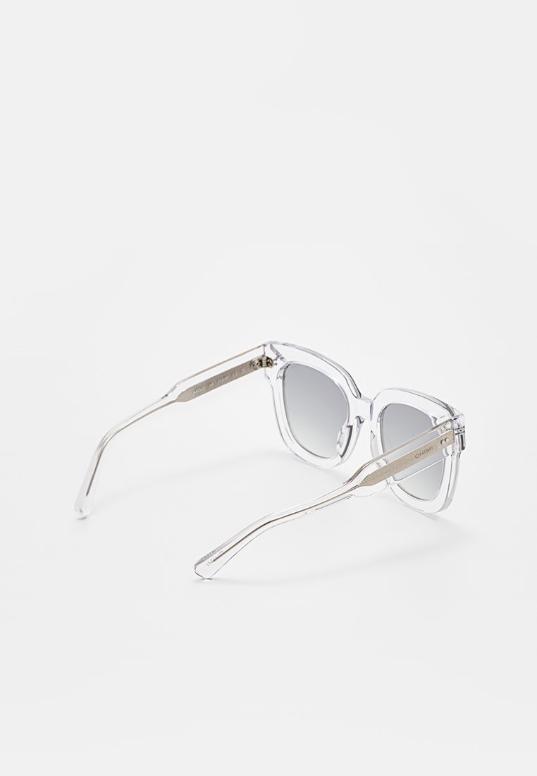 Gafas de sol con marco transparente claro y lentes de degradado gris, con patillas de metal plateado, sobre un fondo blanco.