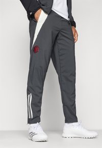 Pantaloni sportivi grigi con accenti bianchi e logo del Manchester United. Presentano una vita elastica, una vestibilità affusolata e tasche laterali.