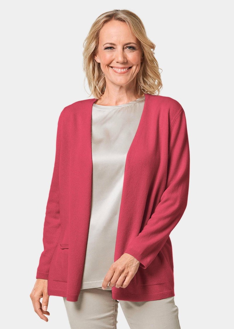 Roze gebreide cardigan met een open voorkant, lange mouwen en twee zakken. Draagt over een licht satijnen top. Zuivere textuur, casual ontwerp.