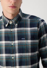 Gombos, kockás ing, amely navy, zöld és fehér kockás mintával rendelkezik, mellzsebével és a zsebnél elhelyezett Barbour logóval.
