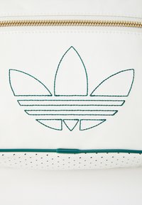 White leather bag with green stitching featuring a trefoil logo. Gold zipper across the top and textured perforated base.