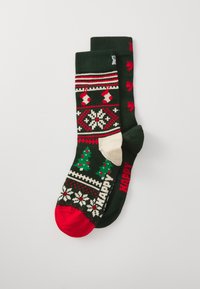 Chaussettes de Noël tricotées avec des couleurs vert foncé, rouge et crème, ornées de motifs d'arbres, de chaussettes et de flocons de neige. Bout rouge et inscription "JOYEUX".