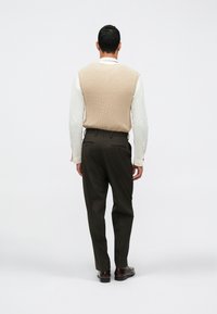 Μπεζ πλεκτό γιλέκο πάνω από λευκό πουκάμισο, συνδυασμένο με σκούρα καφέ παντελόνι και καφέ παπούτσια, με θέα από πίσω. Απλός, υφή σχέδιο.