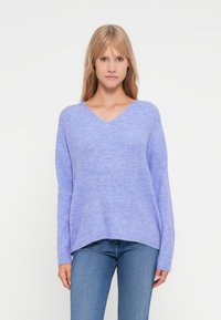 Lys lilla v-hals genser med lange ermer og ribbestruktur, kombinert med blå jeans. Mykt, uformelt design med en avslappet passform.