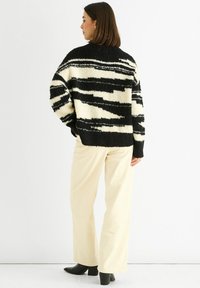 Black and cream patterned sweater with a textured, fuzzy finish and a loose fit, paired with light-colored wide-leg pants and black ankle boots.