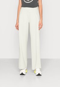 Light grey wide-leg pants with a smooth texture, elastic waistband, and front pockets, paired with white sneakers featuring yellow accents.