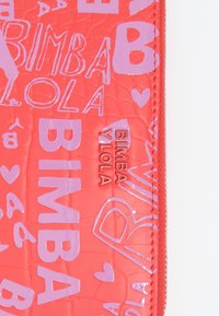 Billetera de charol rojo con texto morado en relieve y diseños de corazones, cierre de cremallera y un patrón texturizado tipo cocodrilo.