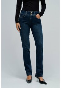 Jeans de talle alto azul oscuro con cinco bolsillos, dos cierres de botón y un diseño de pierna recta, combinados con tacones negros de puntas.