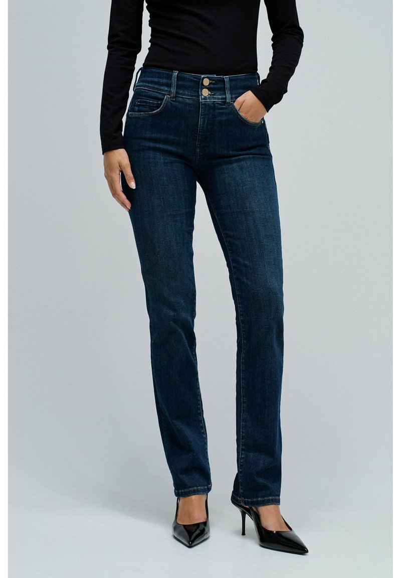 Jeans de talle alto azul oscuro con cinco bolsillos, dos cierres de botón y un diseño de pierna recta, combinados con tacones negros de puntas.