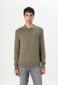 Olivgrünes, gestricktes Polohemd mit langen Ärmeln, zwei Knöpfen und gerippten Bündchen. Leichte Textur, dezentes Logo auf der Brust, gerader Schnitt.