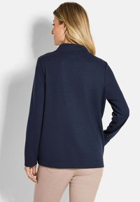 Maglia a maniche lunghe blu navy con colletto, realizzata in un tessuto strutturato. La vista posteriore mostra delle cuciture dritte e una vestibilità rilassata.
