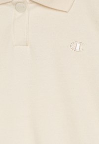 Κρεμ πόλο μπλουζάκι από βαμβάκι με ριχτό γιακά, διαθέτει δύο κουμπιά και κεντητό λογότυπο στο στήθος. Λείος υφή.