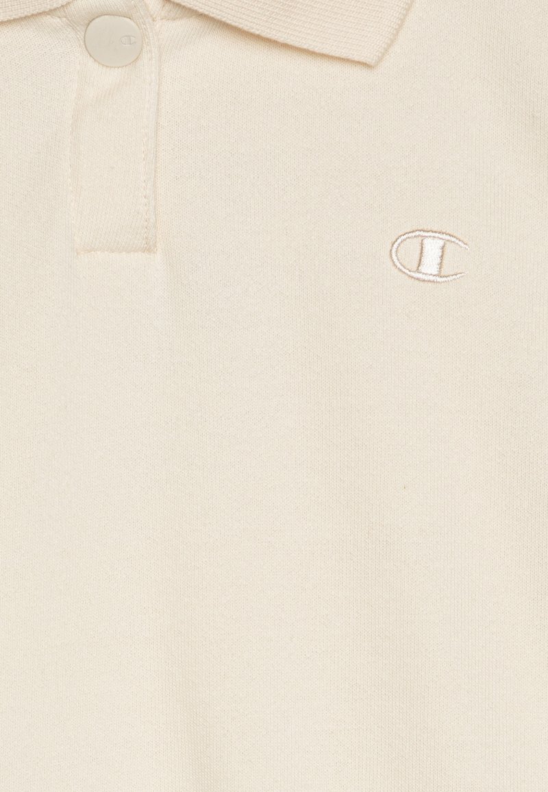 Polo shirt crema in cotone con colletto a coste, dotata di due bottoni e di un logo ricamato sul petto. Texture liscia.