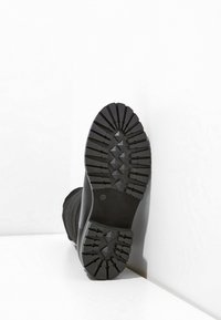 Svart kängasula med robust mönster och diamantformade knölar, slät gummitå, samt texturerad sida för ökad grepp.