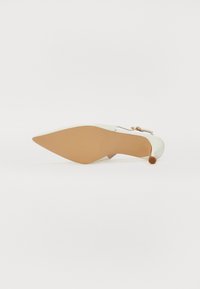 Zapato de tacón alto de cuero blanco con punta afilada y tacón delgado, que presenta un pequeño acento marrón y un detalle de lazo en la parte posterior.