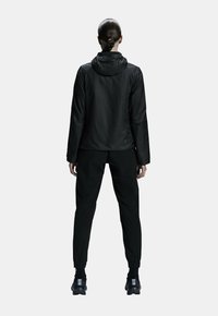Black jacket with a hood and joggers, featuring a smooth texture and elastic cuffs, designed for athletic wear. Seen from the back.