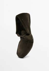 Mocassin en daim marron foncé avec bout cousu, laçage latéral et semelle en caoutchouc, présenté en angle sur un fond blanc.