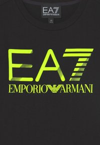 Black cotton t-shirt featuring large neon yellow EA7 and Emporio Armani logos. The logos have varying patterns and textures.