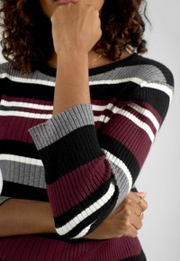 Maglione a coste con strisce orizzontali in bordeaux, nero, grigio e bianco. Le maniche sono aderenti con una leggera svasatura ai polsi.