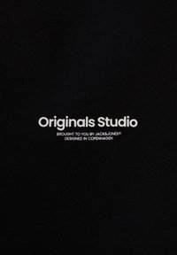 Tessuto nero con testo bianco: "Originals Studio," "Portato a te da JACK&JONES," e "Progettato a Copenhagen." Texture morbida, design minimale.